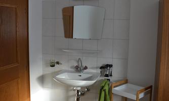 A modern bathroom with a sink and a large mirror. Next to the sink, there is a wooden shelf with towels.