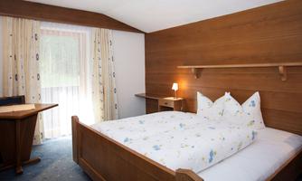A cozy bedroom with wooden paneling and a large bed. There is a desk and a window with curtains.