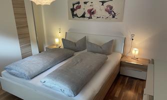 A modern bedroom with a double bed and a neutral color scheme. Soft lighting and decor featuring floral motifs create an inviting atmosphere.
