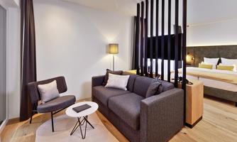 A modern living ambiance with a gray sofa and a chair. The room has a bright, friendly atmosphere and is structured by a partition wall.