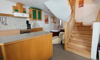 A modern kitchen with wooden shelves and an open staircase. The room is brightly and invitingly designed.