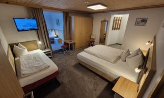 A cozy hotel room with two beds and a television. There is a table and a wardrobe, as well as a bright and friendly room.