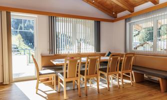A modern dining room with a wooden table and chairs. Large windows let in plenty of light and offer a view of the surroundings.