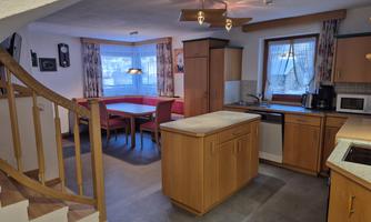 A modern kitchenette with wooden furniture and a cozy dining area. The large windows let in plenty of daylight.
