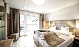 A modern bedroom with a cozy double bed and soft colors. Large windows allow plenty of light and a view of nature.