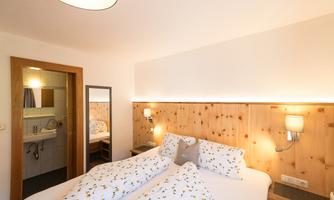 A cozy bedroom with two beds and wood paneling. There is a bathroom and a mirror nearby.