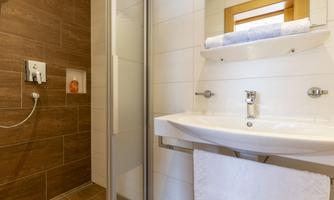A modern bathroom with a shower and a sink. The wall tiles are bright, and there is a wooden surface for a warm atmosphere.