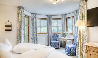 A cozy room with two beds and large windows. The decor is bright and cheerful, with blue curtains and a small table.