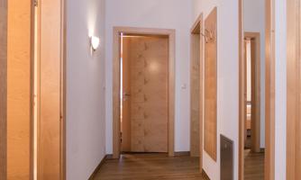 A bright hallway with wooden flooring and white walls. Two mirrors are on the walls, and a door leads to another room.