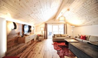 A cozy living room with wooden floors and a high ceiling. The decor is modern and stylish, complemented by large windows that let in plenty of light.