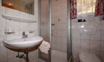 A small bathroom with a shower, sink, and toilet. Bright tiles and a window provide light and a friendly atmosphere.