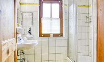 A small bathroom with a shower and a sink. There is a roller shutter at the window, and the walls are tiled.