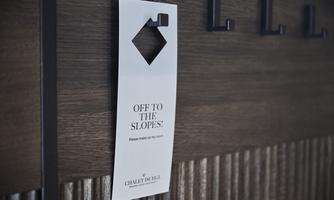 A note hangs on a wooden board indicating that the room should be cleaned. The text reads: “Off to the slopes! Please make my room.”