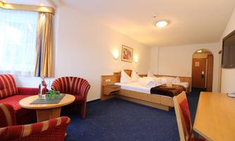 A cozy hotel room with a double bed and two single beds. The room has a table with chairs and a television.