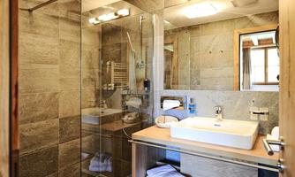 A modern bathroom with a glass shower and wooden shelf. Bright tiles and a large sink create an appealing atmosphere.