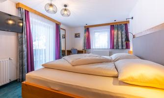 A cozy room with a large bed and colorful curtains. There is a television and plenty of natural light coming through the windows.
