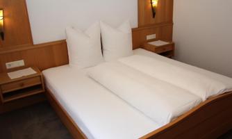 A cozy bedroom with a large bed and two pillows. The walls are in warm wood tones, and there are nightstands on both sides.