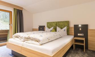 A cozy bedroom with a large double bed and soft pillows. The walls are in warm wood tones, and there is a balcony with a view outside.