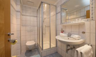 A modern bathroom with a shower and a sink. It is clean and brightly tiled with towels ready.