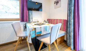 A cozy dining area with a table and two chairs. The walls are adorned with purple curtains and modern decoration.