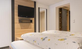A modern bedroom with a double bed and multicolor floral bedding. There is a television on the wall and a large mirror.