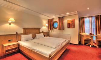 A modern hotel room with two single beds and a cozy table. The room features warm colors and plenty of daylight.