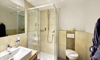 A modern bathroom with a glass shower and a sink. The walls are in neutral colors, and there is an elegant toilet area.