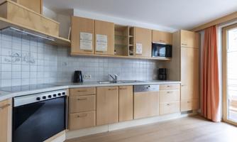 A modern kitchen with wooden cabinets and white tiles. It is bright and well-equipped with appliances such as a stove, microwave, and coffee maker.