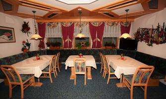 A cozy restaurant with bright tables and colorful chairs. The atmosphere is inviting with pretty curtains and plants.