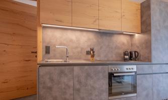 A modern kitchen with wood and gray tones. It is well-equipped with a sink, stove, and kitchen appliances.