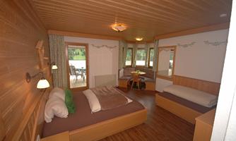 A cozy room with wood paneling and two beds. Large windows let in plenty of daylight and offer a view outside.
