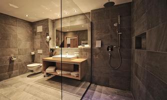 A modern bathroom with gray tiles and a spacious shower. The large mirror and the wooden shelf add an elegant touch to the space.