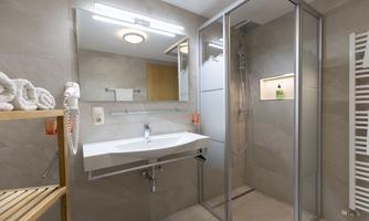 A modern bathroom with a shower cubicle and a large sink. Towels are neatly placed on a wooden shelf.