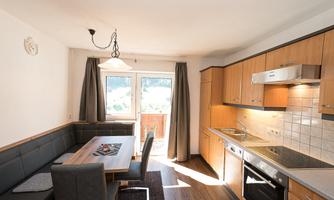 A modern kitchen with wooden cabinets and a dining area. Large windows let in plenty of daylight.