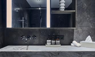 A modern bathroom with an elegant marble washbasin and a lit mirror. On the shelf, skincare products and fresh towels are arranged.