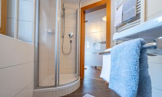 A modern bathroom with a shower cabin and large tiles. Towels are hanging on a towel rack nearby.