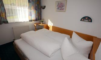 A cozy room with a double bed and large pillows. The room has a window with curtains and a small table.