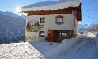 A cozy house in the snow with a picturesque mural. The surrounding landscape features majestic mountains and a blue sky.
