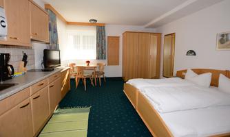 A cozy room with a double bed, table, and chairs. The kitchen is well-equipped and a window provides plenty of light.