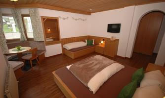 A modern room with wooden furniture and a bright design. The room features two beds, a TV, and a small seating area.