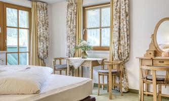 A cozy room with a large bed, a table, and chairs.  
Large windows with curtains provide plenty of daylight.