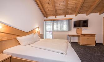 A modern bedroom with a large bed and wooden beam ceiling. There is a television and a desk in the room.
