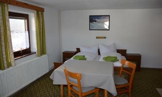 A simple room with two beds and a table. There is a window with curtains and a wall color in neutral tones.