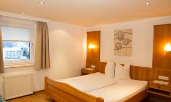 A cozy bedroom with a double bed and light wooden paneling. The window lets in daylight and creates a pleasant atmosphere.
