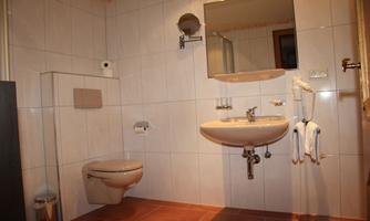 A modern bathroom with a toilet, a sink, and a mirror. White tiles and brown flooring create a bright atmosphere.