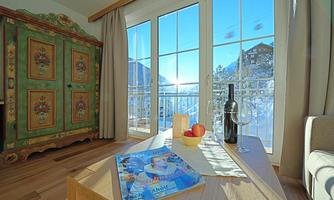 A cozy living space with large windows overlooking snow-covered mountains. On the table are a magazine, a glass of wine, and apples.