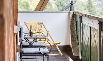 A cozy balcony with two chairs and a table. On the table, there is a bottle of champagne and glasses, surrounded by a beautiful view.