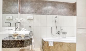 A modern bathroom with a bathtub and a shower. The walls are in neutral colors, and there is an elegant washbasin made of black marble.