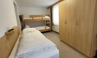 A simple room with a single bed and a bunk bed. The room is bright and friendly, with a large wardrobe and a carpet.
