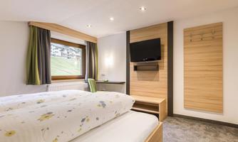 A modern bedroom with two beds and a television on the wall. Large windows provide plenty of daylight and a view outside.